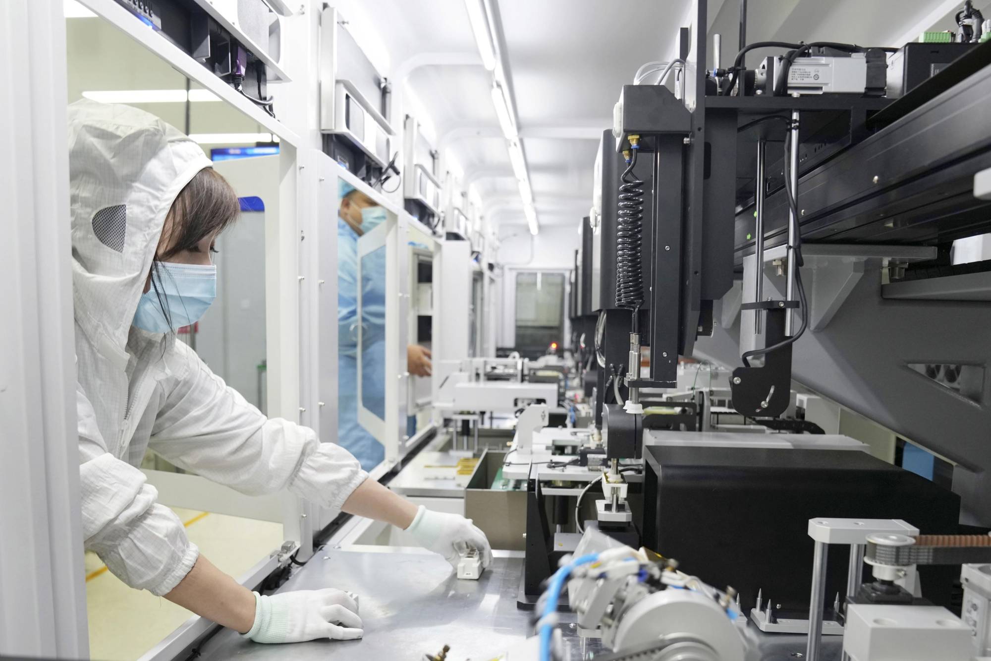 a woman in a white coverall and protective mask working in a factory