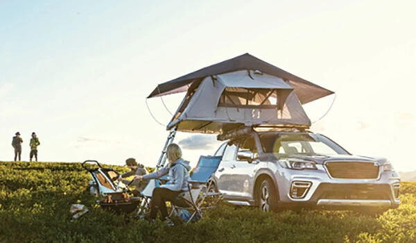 Family sits on a grassy hill next to a Thule camper mounted on an SUV